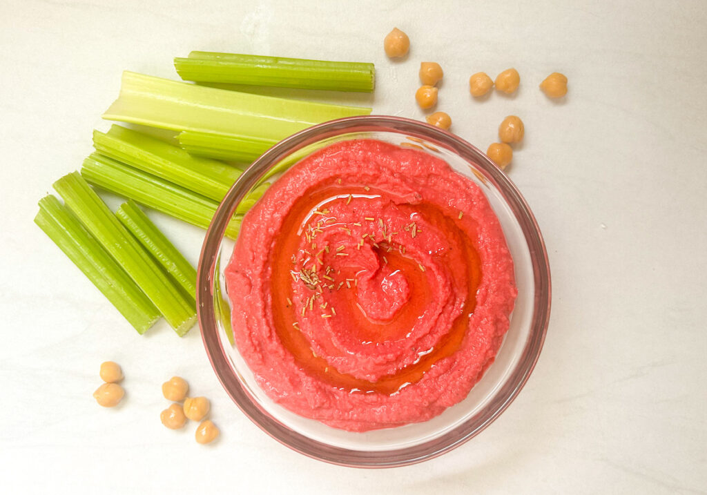 beet hummus in a bowl with celery sticks