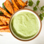 green goddess herb dip in a white bowl with roasted sweet potatoes to dip