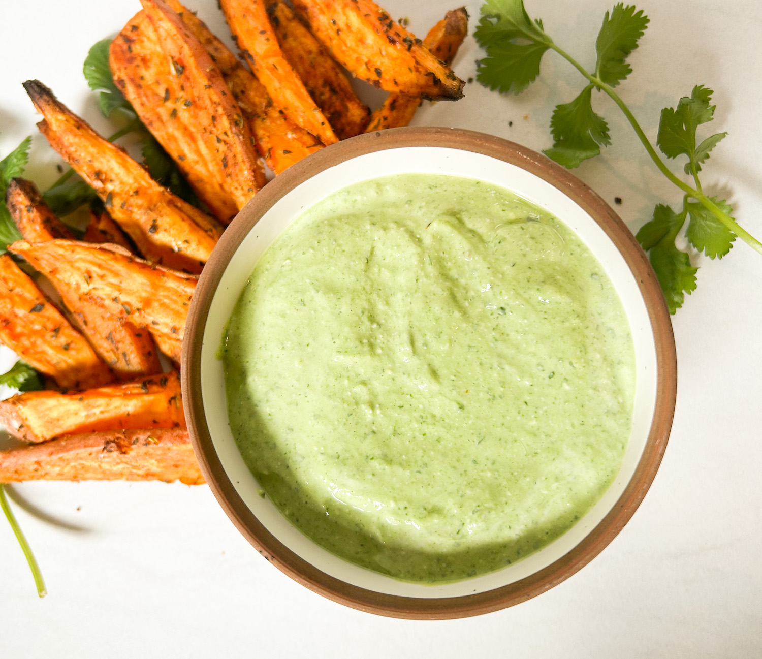 green goddess herb dip in a white bowl with roasted sweet potatoes to dip