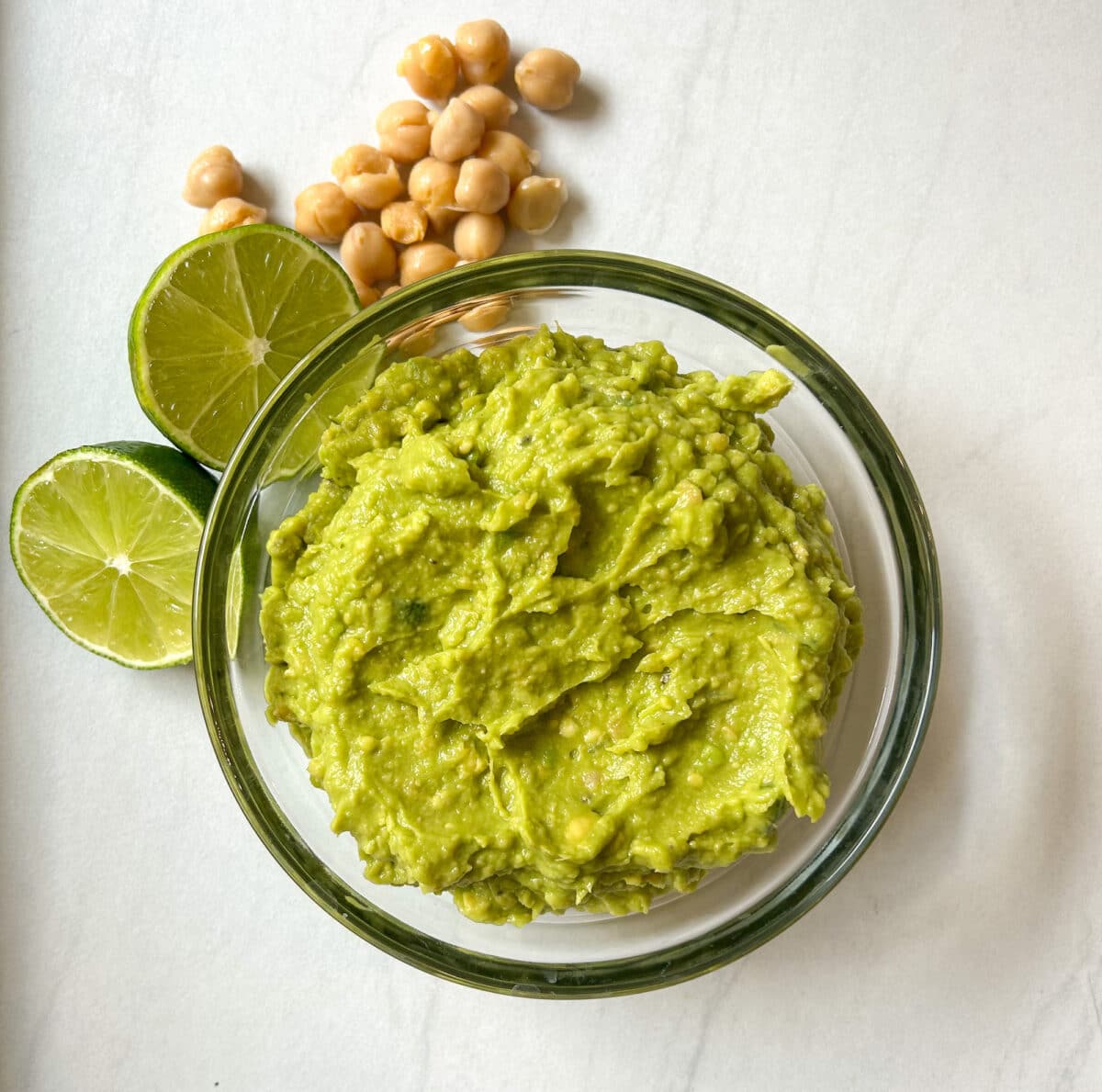 Guacamole in a glass bowl with lime and chickpeas