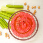 beet hummus in a bowl with celery sticks